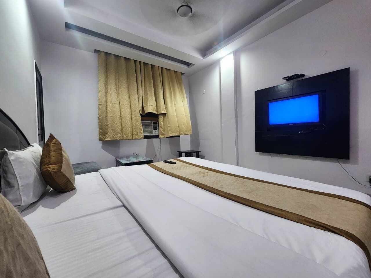 A hotel room with a bed, a TV mounted on the wall, and a window with curtains.