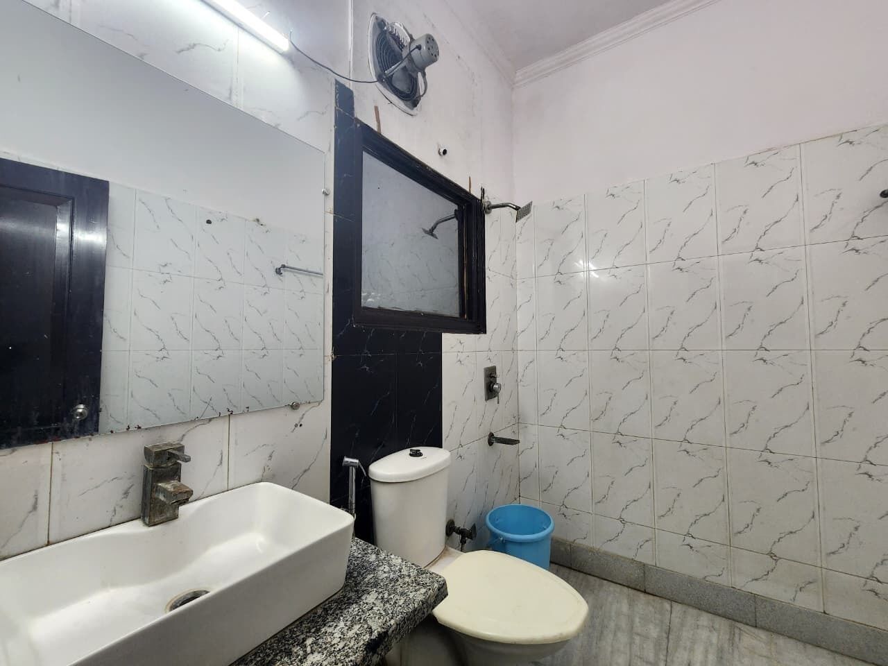 A bathroom with a white sink, a toilet, and a blue trash bin.
