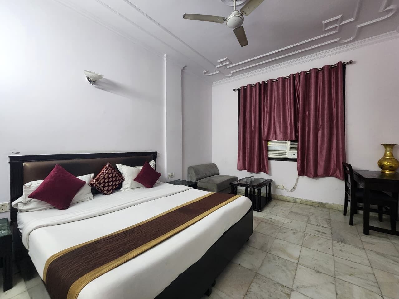 A hotel room with a large bed, a desk, a chair, a ceiling fan, and a window with curtains.