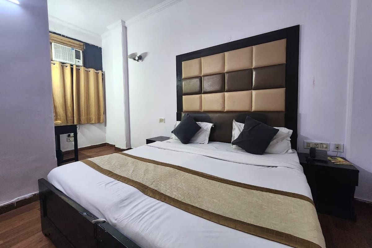 Une chambre d’hôtel avec un grand lit, une tête de lit dotée d’un panneau rembourré, une table de chevet avec une lampe et une fenêtre avec des rideaux.