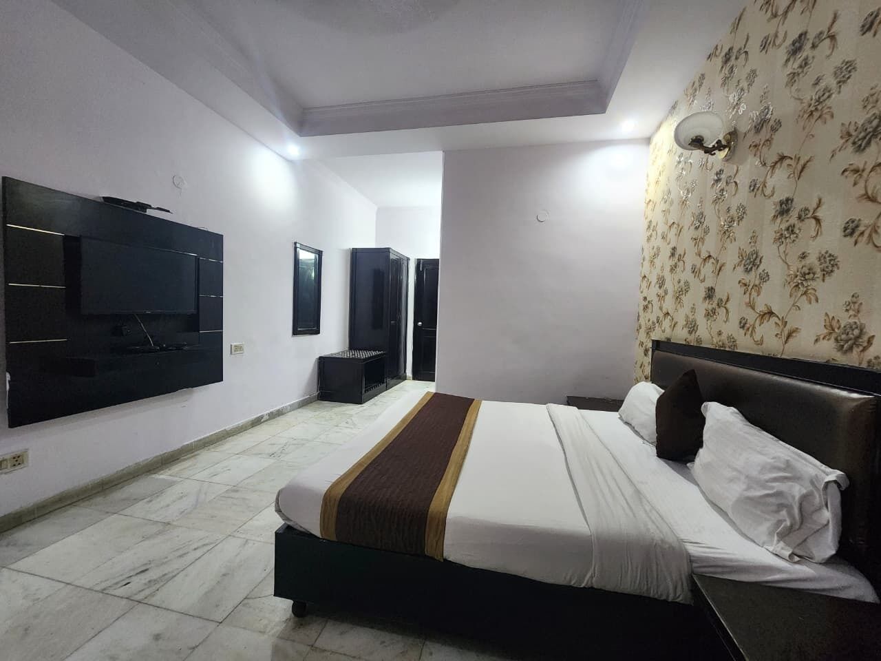 A hotel room with a bed, a television mounted on the wall, and a patterned wallpaper on one wall.