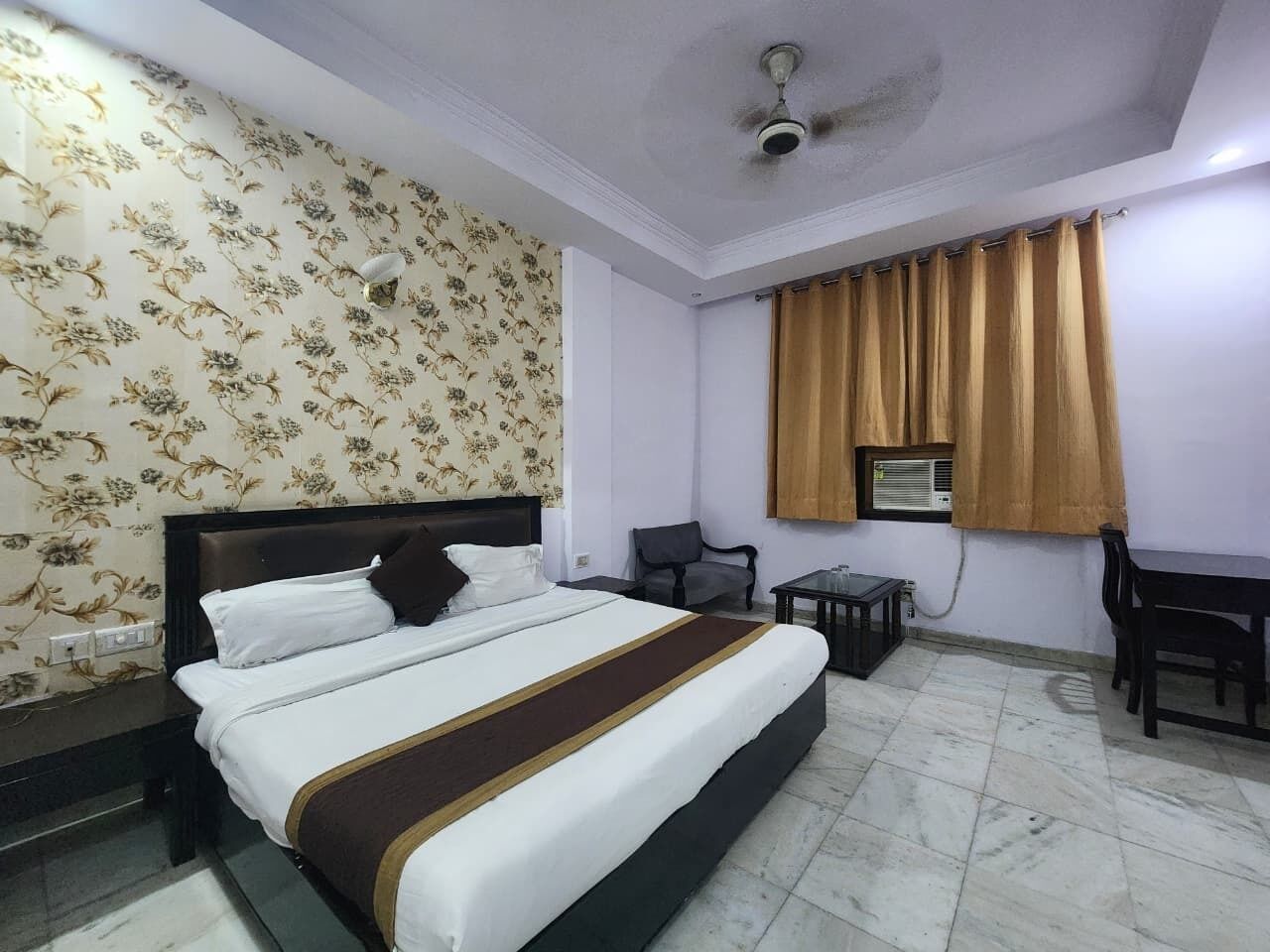 Una habitación de hotel con cama, escritorio, silla, ventilador de techo y ventana con cortinas.