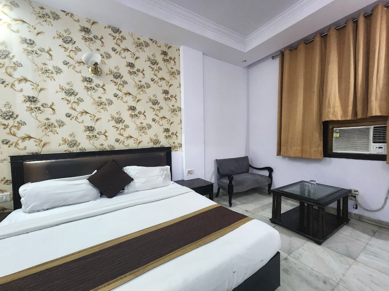 A hotel room with a bed, a chair, a small table, and a window with curtains.