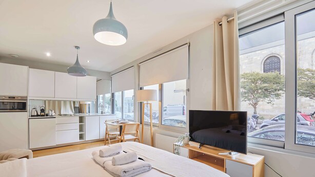 Een moderne hotelkamer met een groot bed, een televisie, een bureau en uitzicht op de straat door grote ramen.