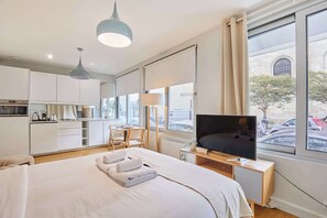 Une chambre d’hôtel moderne dotée d’un grand lit, d’une télévision, d’un bureau et offrant une vue sur la rue grâce à de grandes fenêtres.