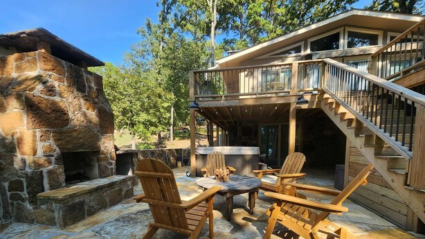 A stone fireplace, wooden deck, outdoor seating, and a staircase leading to a covered area.