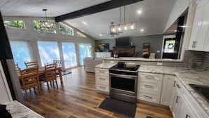 A modern kitchen with wooden flooring, white cabinets, and a large window overlooking a green landscape.