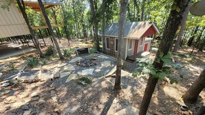 A rustic cabin surrounded by trees, with a stone patio and a small fire pit.