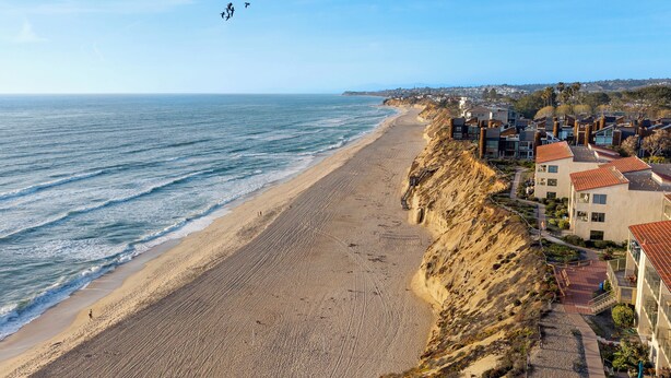 A coastal residential area with a beach, houses with red roofs, and a clear sky.