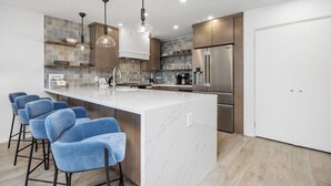 A modern kitchen with a marble island, stainless steel appliances, and blue bar stools.