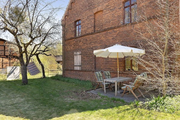 A brick building with a patio area featuring a table and chairs, an umbrella, and a tree.