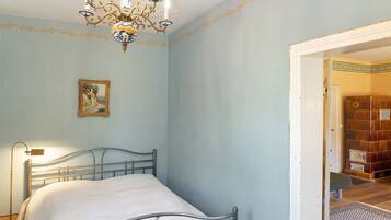 Un dormitorio con cama, candelabro, un cuadro y una puerta que da a otra habitación.