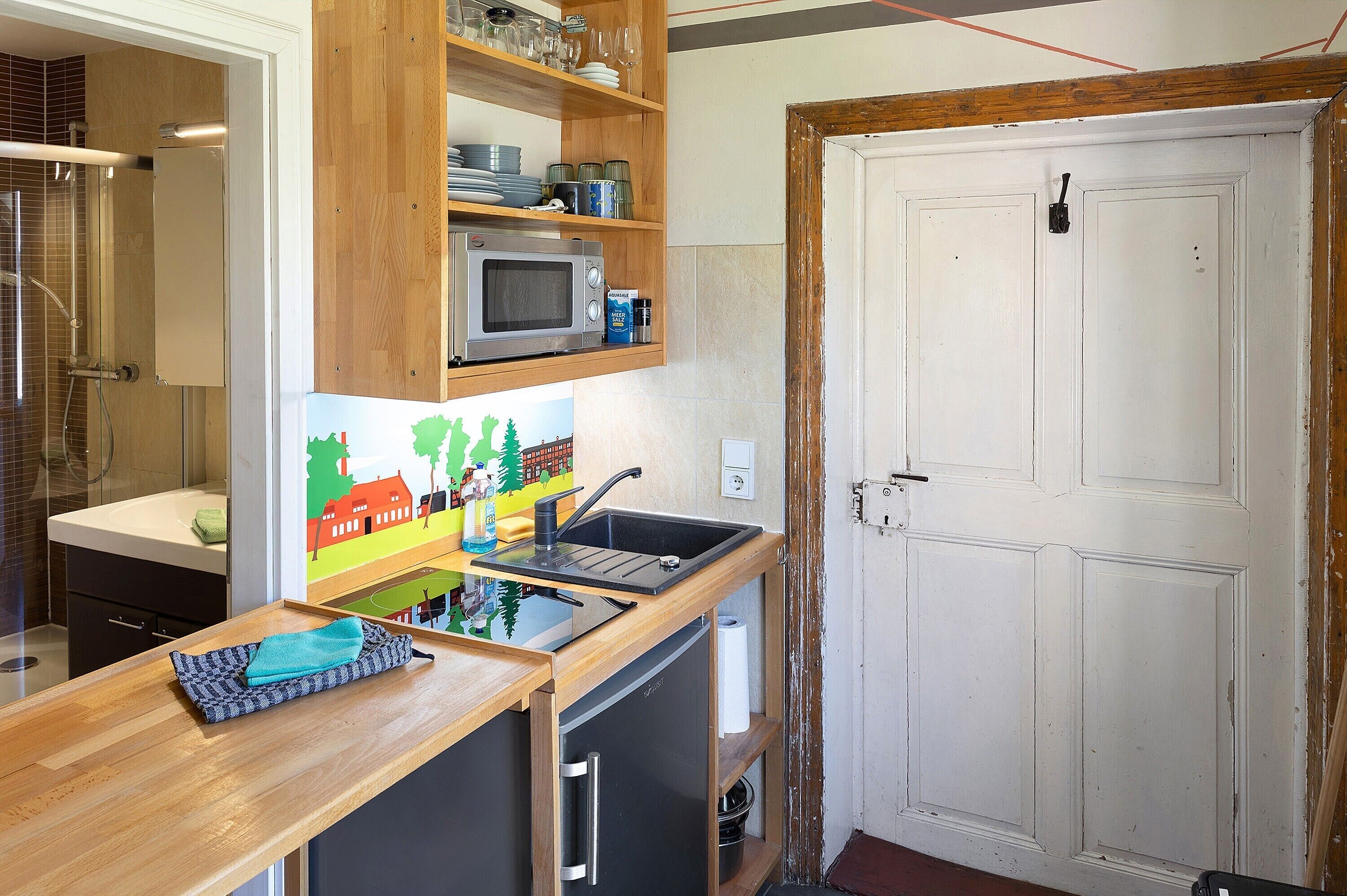 Una cocina con microondas, estantes de madera, un lavabo y una puerta.
