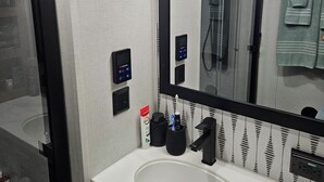 A modern bathroom with a white sink, black faucet, and a large mirror. There are two toothbrush holders and a tube of toothpaste on the counter.