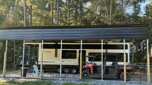 A covered RV with a 'Wildwood Grand Lodge' sign, a red ATV, and a covered seating area with chairs.