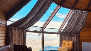 Una habitación acogedora con techo inclinado, ventanas grandes, suelo de madera, una silla y una cama.