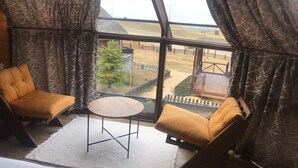 Una habitación con dos sillas amarillas acolchadas, una mesita redonda y vistas a un espacio exterior cercado con un árbol y una terraza de madera.