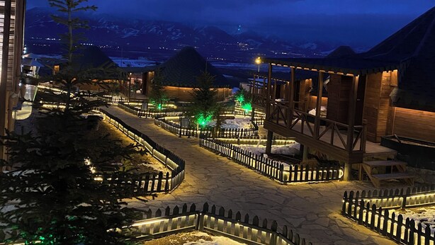 Un patio cubierto de nieve con una cerca de madera, un edificio de madera y una vista de la montaña al fondo.