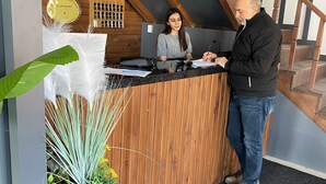 Un mostrador de recepción con detalles de madera, suelo cubierto de alfombra negra y una escalera al fondo.