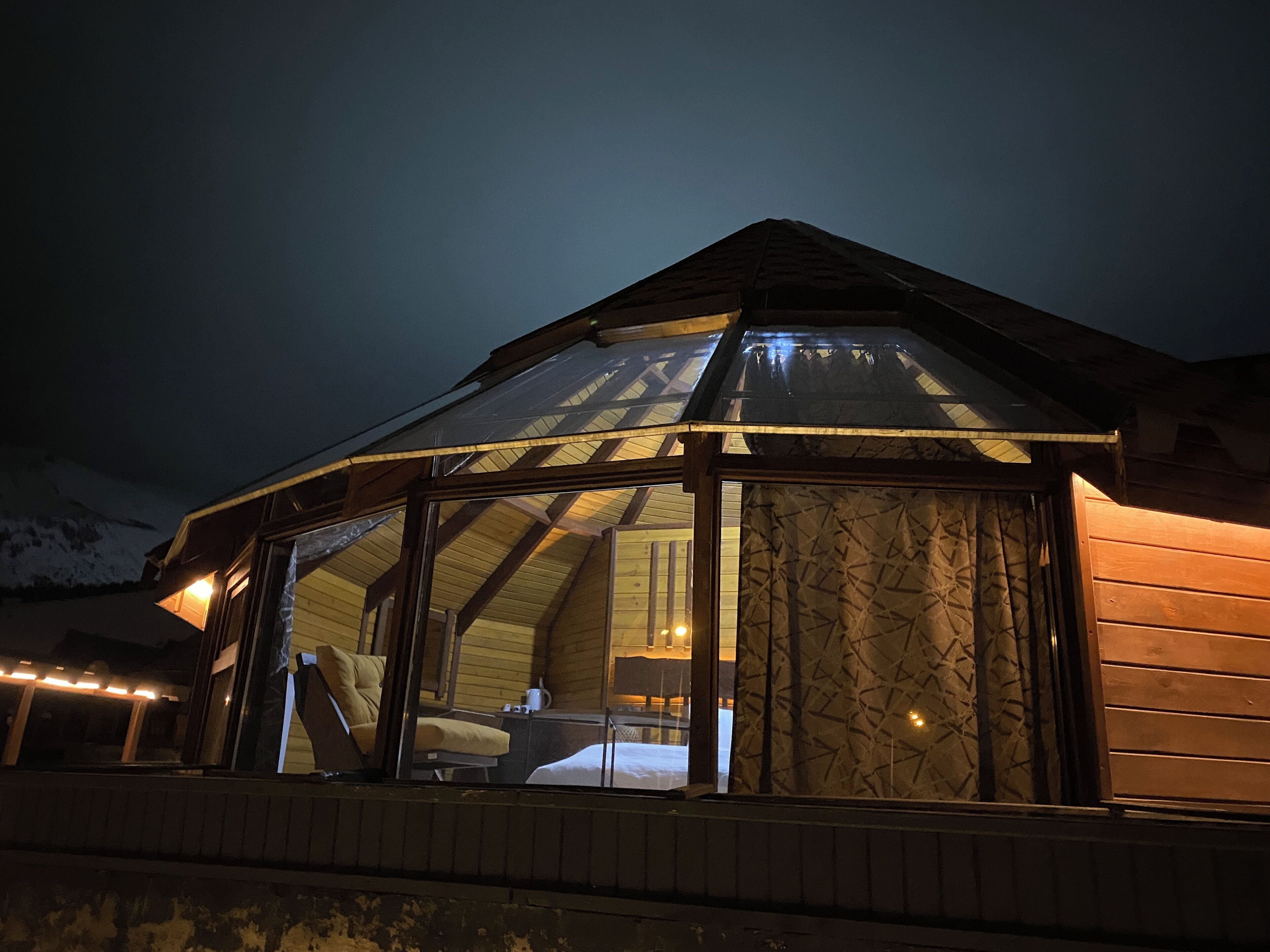 A wooden cabin with a large glass window, a bed, and a chair.