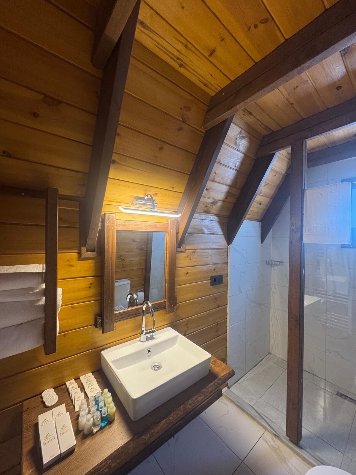A wooden cabin bathroom with a sink, mirror, and shower.