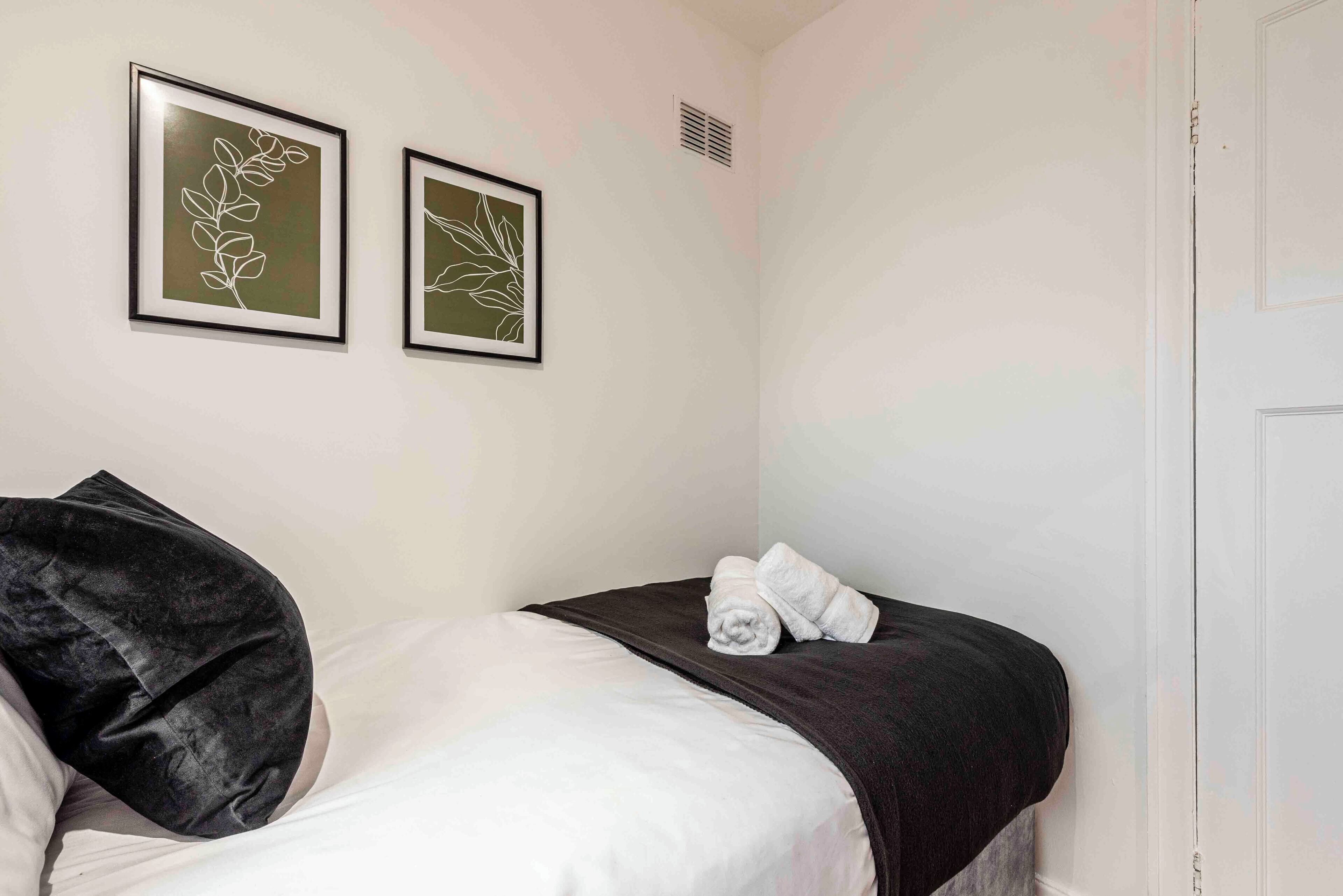 Habitació d'hotel amb llit, almoina negra, dues obres d'art emmarcades i una porta blanca.