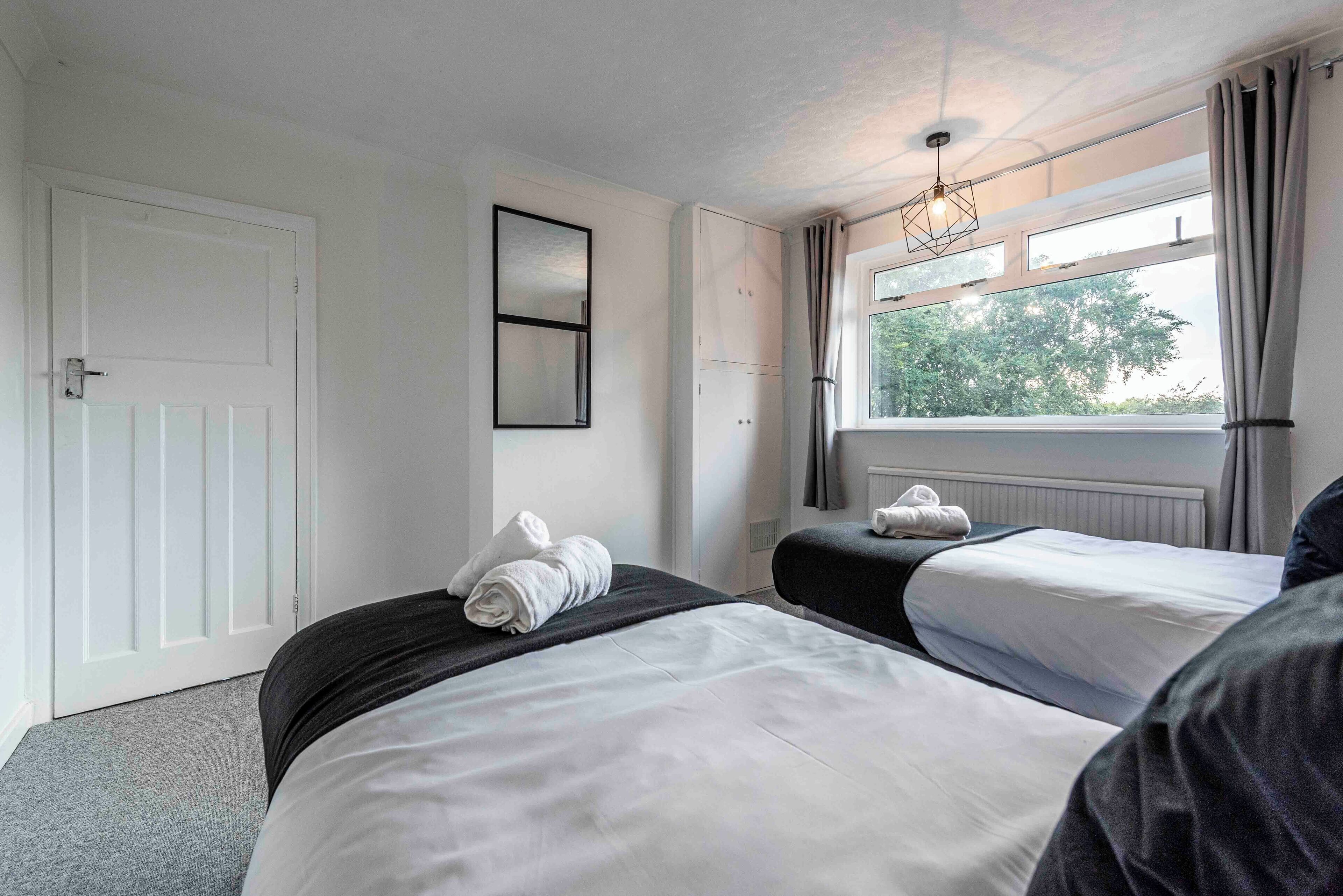 A hotel room with two beds, a window with curtains, a door, and a mirror on the wall.
