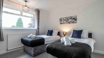 Ett hotellrum med två sängar, ett fönster med gardiner, ett element och konst på väggen.