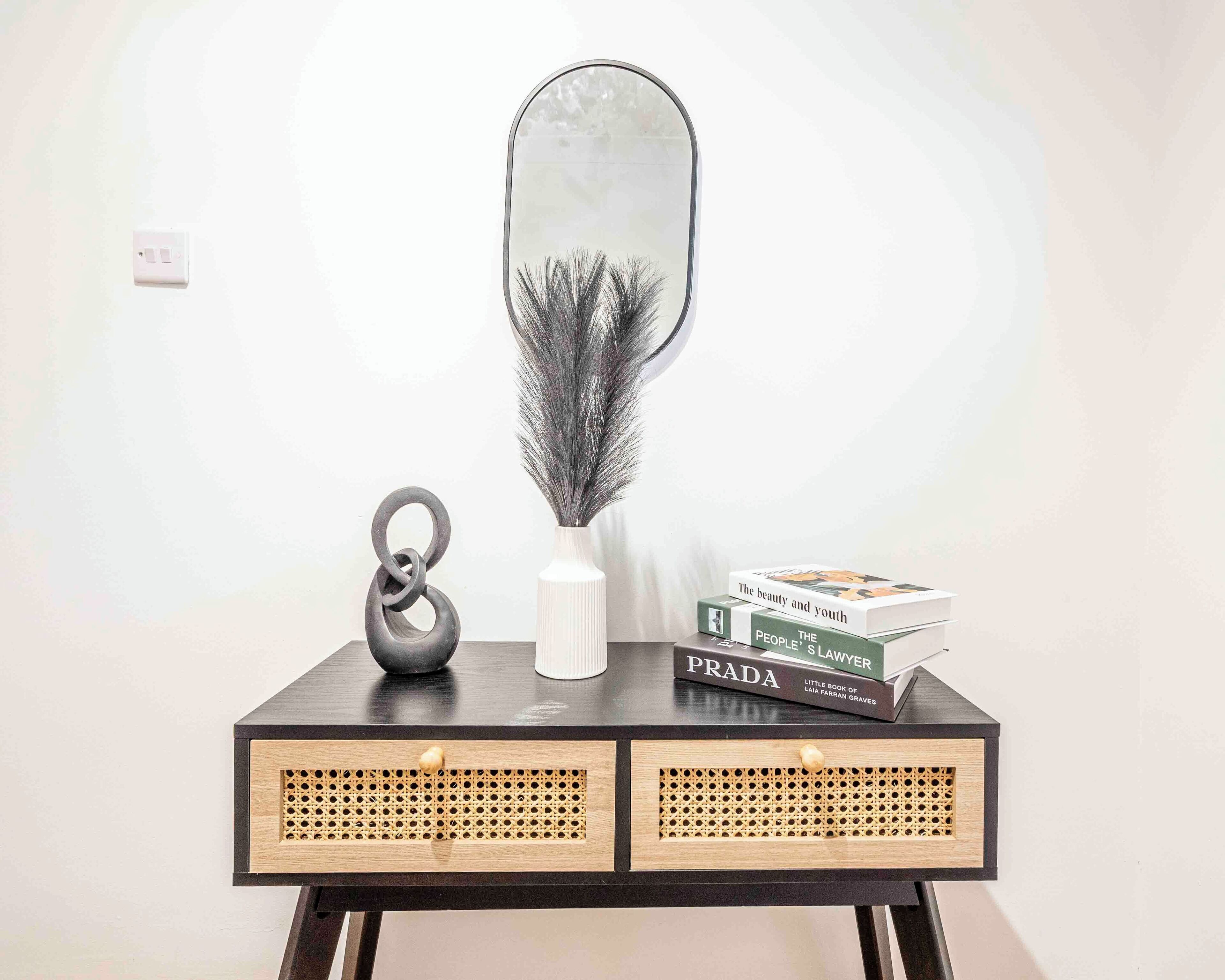 A small black console table with a mirror, a decorative vase, and a stack of books.