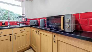 Une cuisine avec des meubles de rangement en bois, un plan de travail noir, un grille-pain, une bouilloire et un four à micro-ondes.