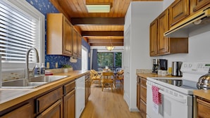 A kitchen with wooden cabinets, a white dishwasher, a dining area with a table and chairs, and a view of the outdoors through a window. - Snowflake Chalet -Govy Chalet Steps to Glade Trail (Government Camp)
