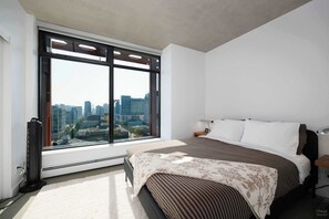 Un dormitorio con un ventanal grande, una cama, una mesita de noche y una lámpara fijada a la pared.