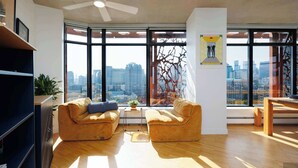 Un moderno salón con vista a la ciudad, un ventilador de techo y un ventanal grande.