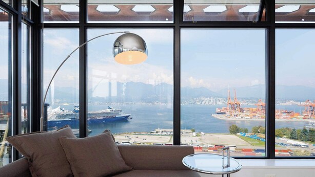 Una habitación moderna con un ventanal grande, un sofá, una mesita y una lámpara de pie.