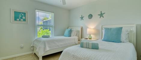 Camera da letto con due letti, una ventola a soffitto, una finestra con persiane e stelle marine decorative al muro.