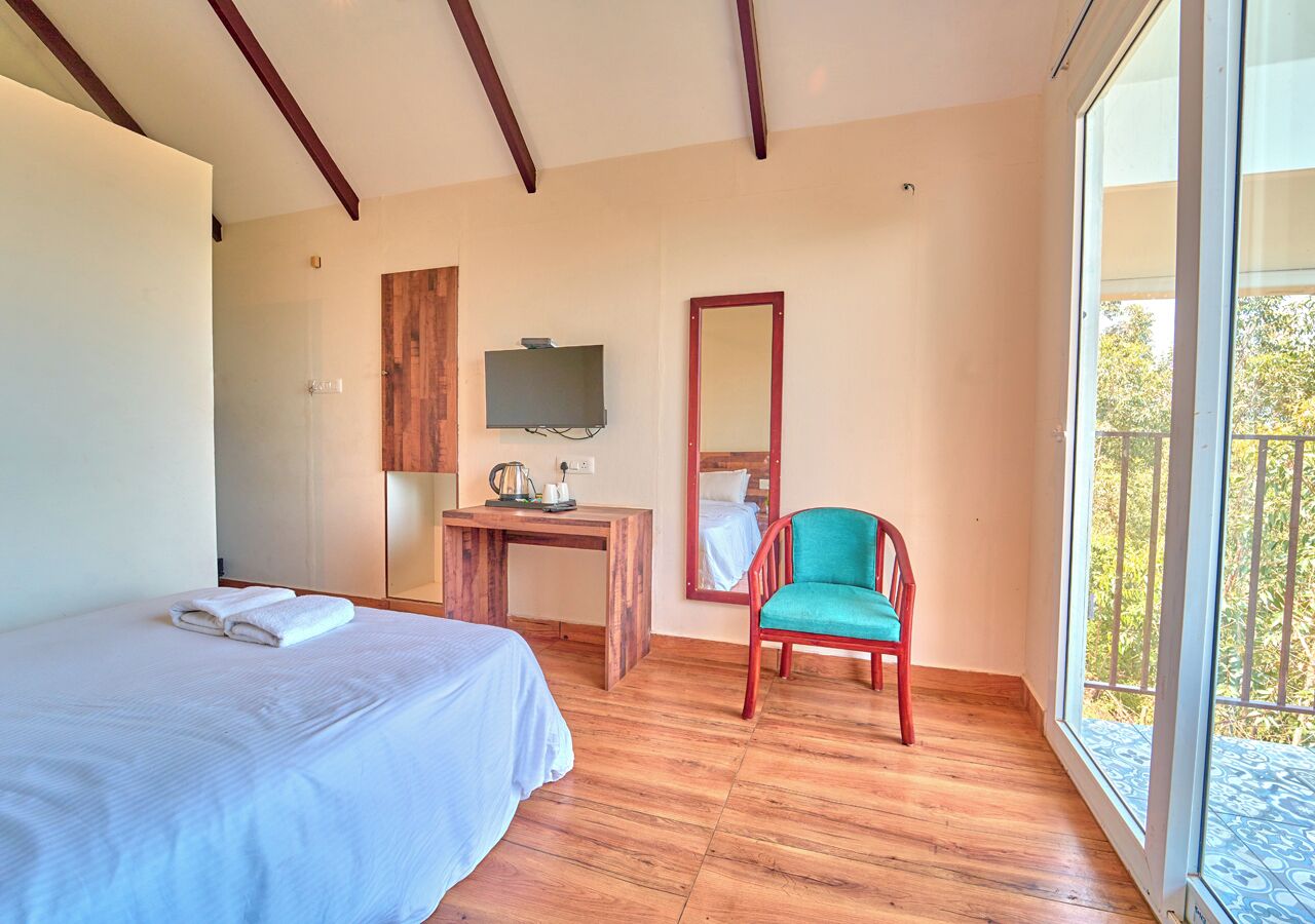 A bedroom with a bed, a desk, a chair, a TV, and a balcony with a view.