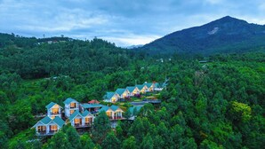 A cluster of modern, multi-story houses with large windows, surrounded by dense forest and a mountain in the background. - Gardenia Kanthalloor by VOYE HOMES (Devikolam)