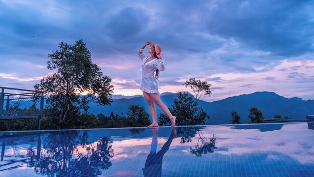 A person standing on a reflective infinity pool with a mountainous landscape in the background. - Gardenia Kanthalloor by VOYE HOMES (Devikolam)