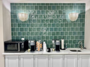 A kitchen with a green tiled backsplash, a microwave, a coffee maker, a kettle, and a sink. - Blue Bliss Seawall | Gulf Views • Walk to Beach (Galveston)