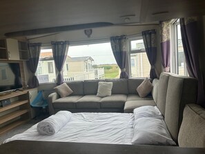 A bedroom with a bed, a sofa, a TV, and a window with curtains. - Familycaravan-seaview-garden-ensuite-nearbeach (Clacton-on-Sea)