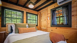 A wooden cabin bedroom with a large bed, two windows, and a ceiling fan. - Intimate Cabin Escape: Hot Tub, Sauna, Firepit, Grill & Projector (Mentone)