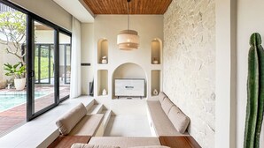 A modern living room with a large TV, built-in seating, and a stone wall. - 2-bedroom Villa Athaya in peaceful Bali (Bali)