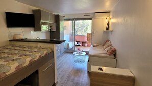 A compact room with a bed, a desk, a chair, and a small table. There is a sliding door leading to an outdoor area.