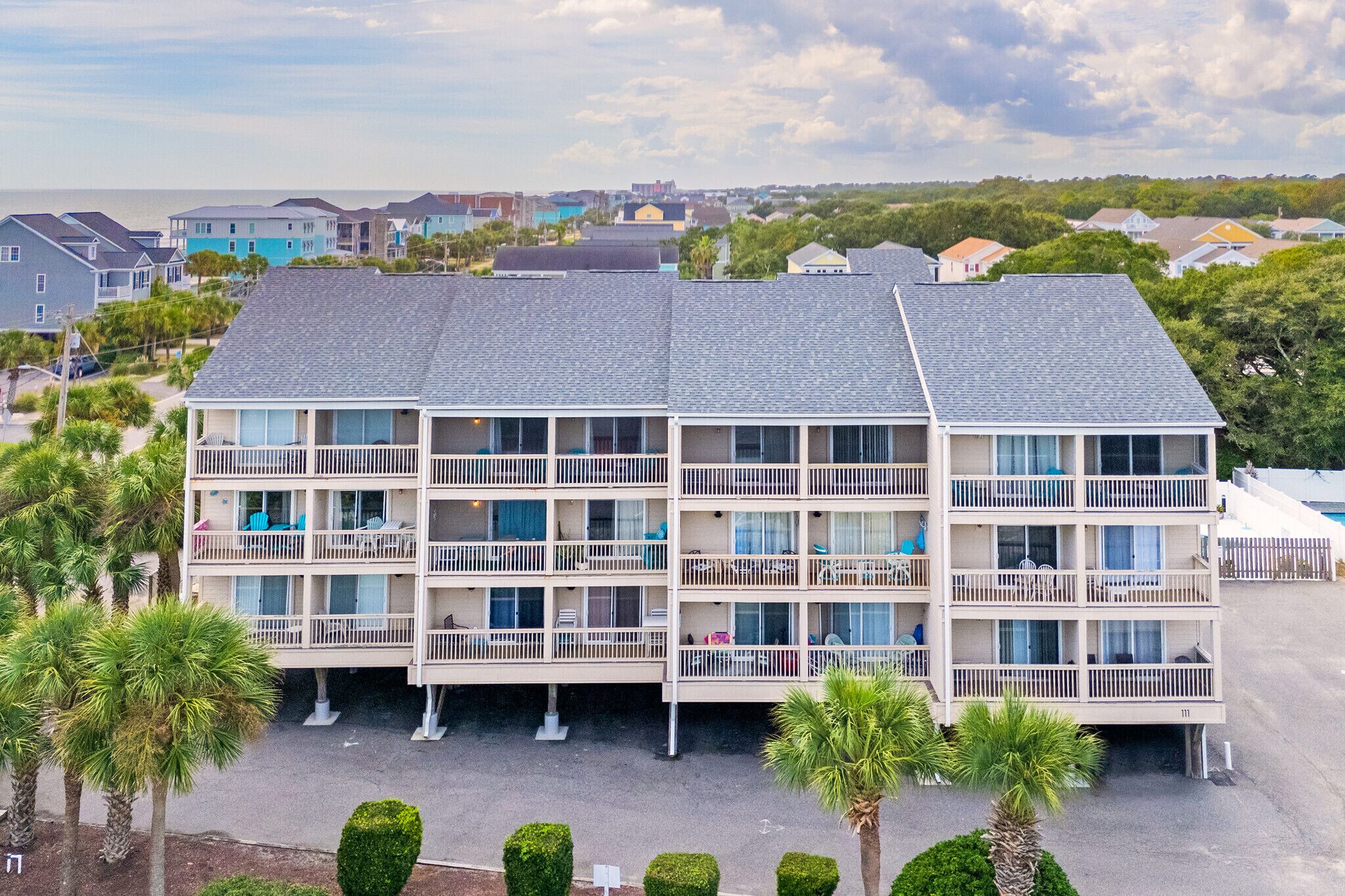 A multi-story hotel with balconies, a parking area, and a view of the sea.