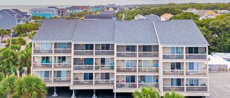 A multi-story hotel with balconies, a parking area, and a view of the sea.