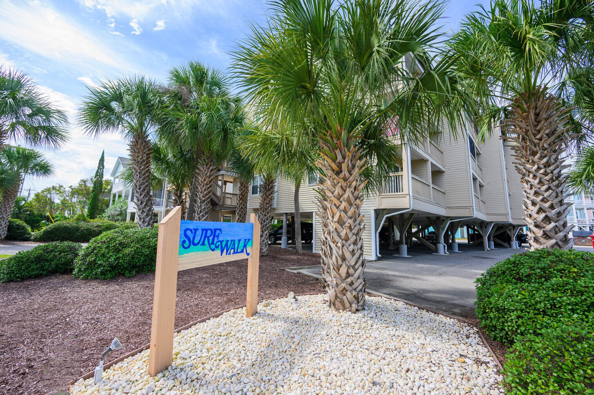 A sign for a 'Sea Walk' path, palm trees, and a building with a covered walkway.