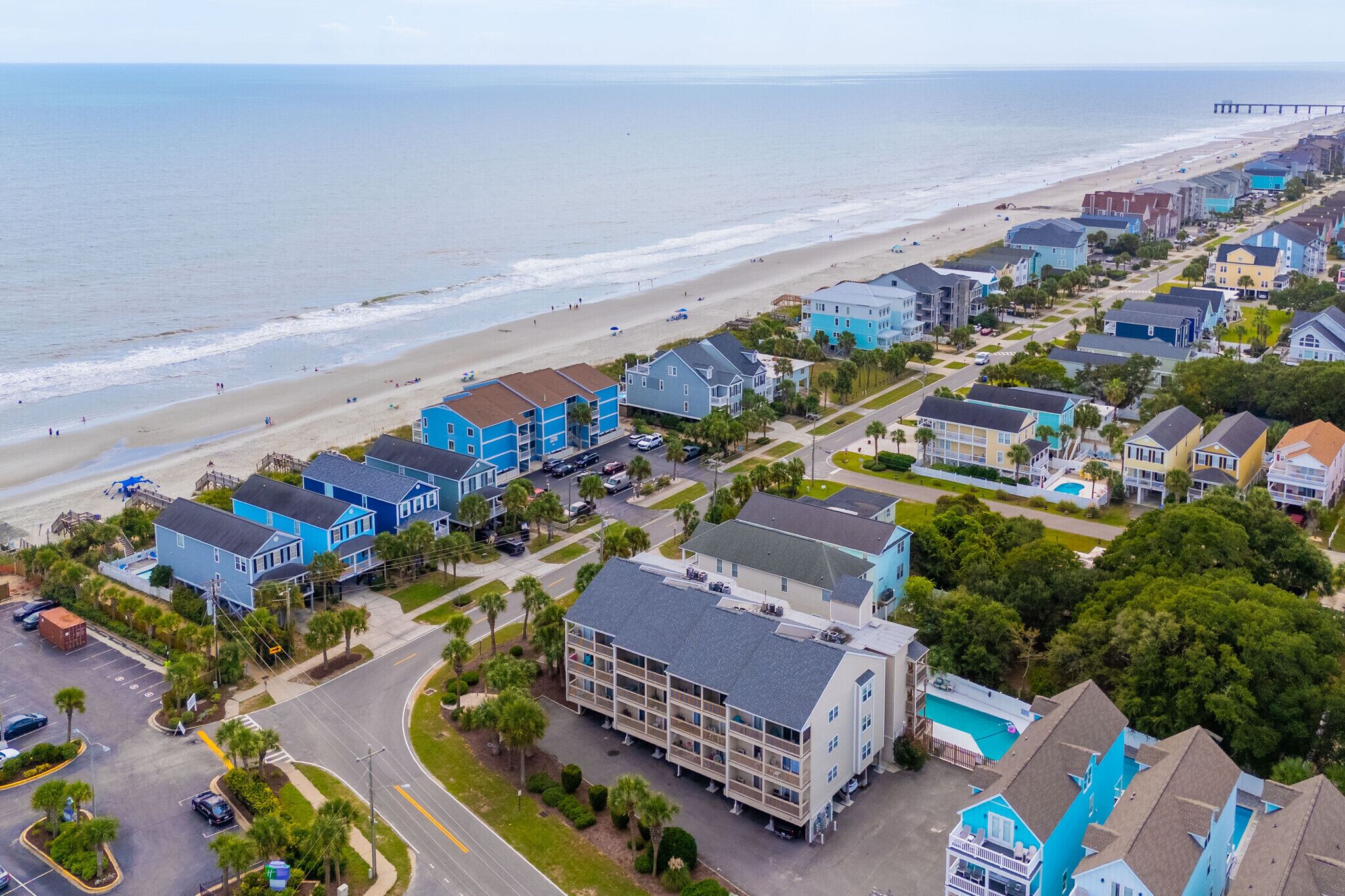 An aerial view of a coastal residential area with houses, a beach, and a pier.