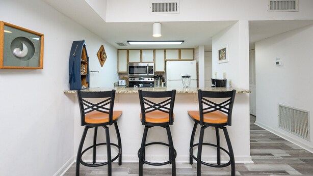 A modern kitchen with a central island, three bar stools, and a microwave. - Surfwalk 343 – Shared Pool, 2 Balconies & Easy Beach Access (Surfside Beach)