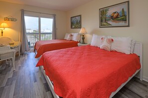 Een hotelkamer met twee bedden, een balkon, een rieten stoel en een schilderij aan de muur.