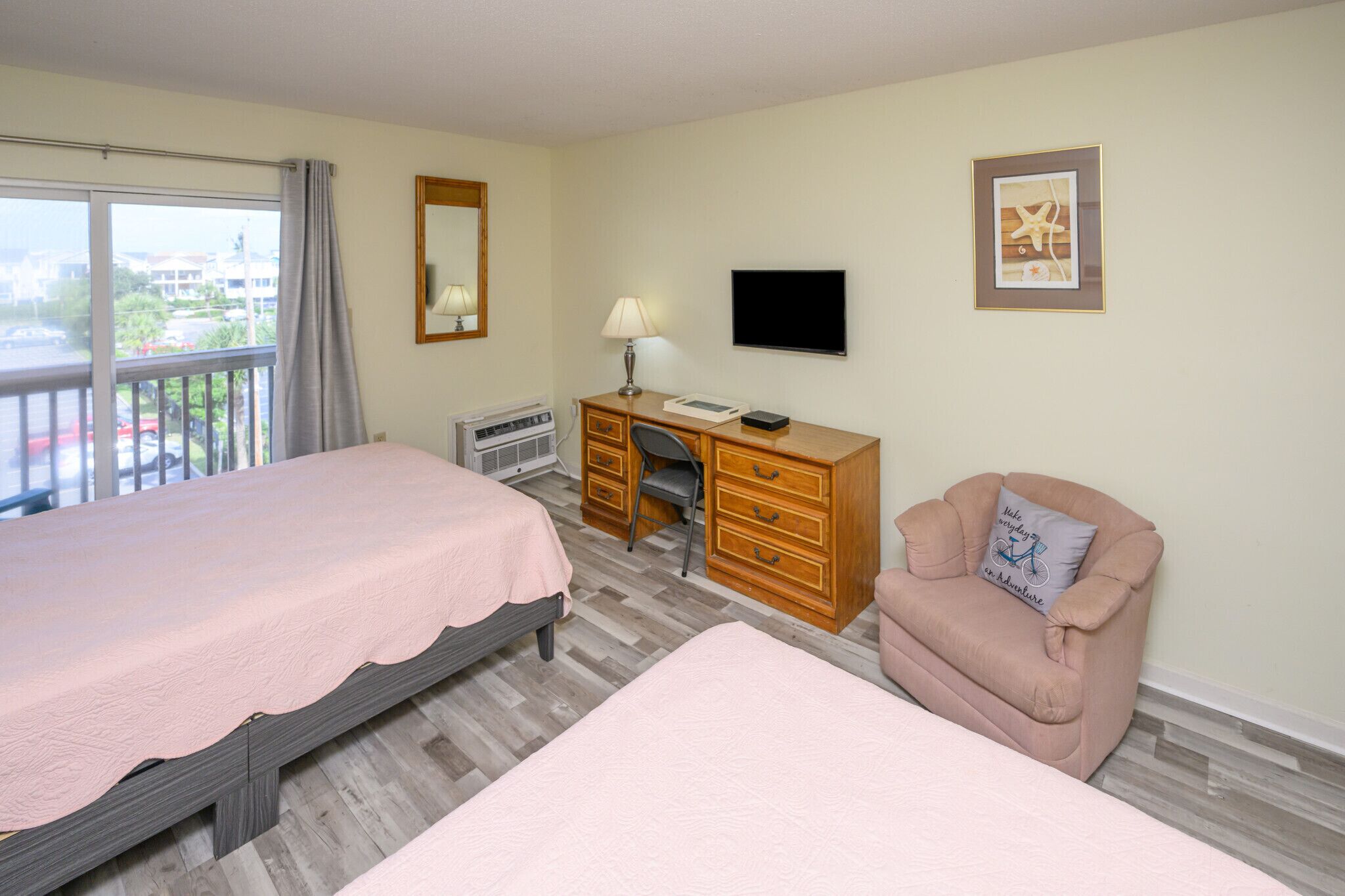 A hotel room with two beds, a desk, a chair, a television, and a window with a view of buildings.